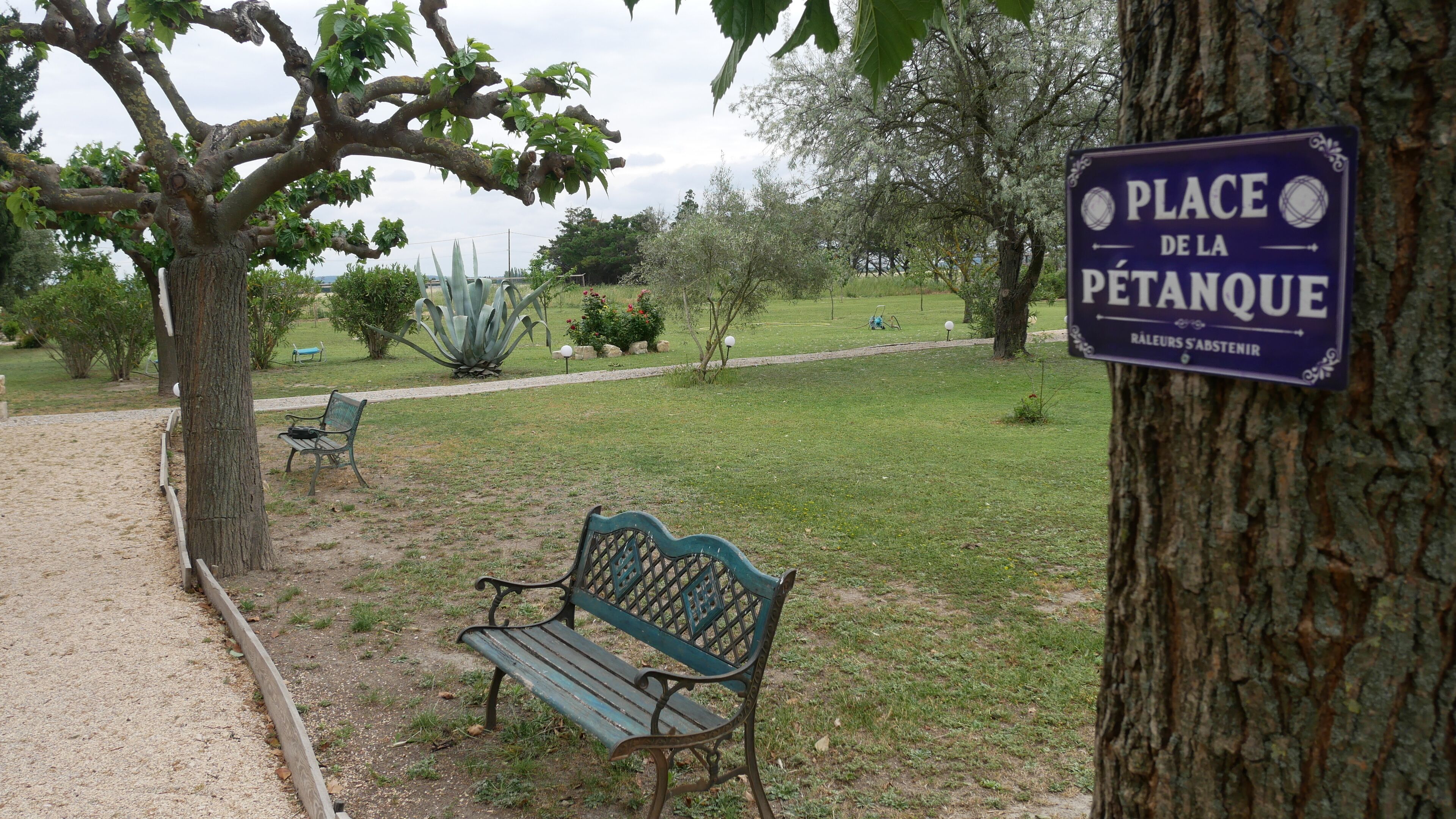 Un parque con un cartel que dice 'PLACE DE LA PETANQUE' y un banco.