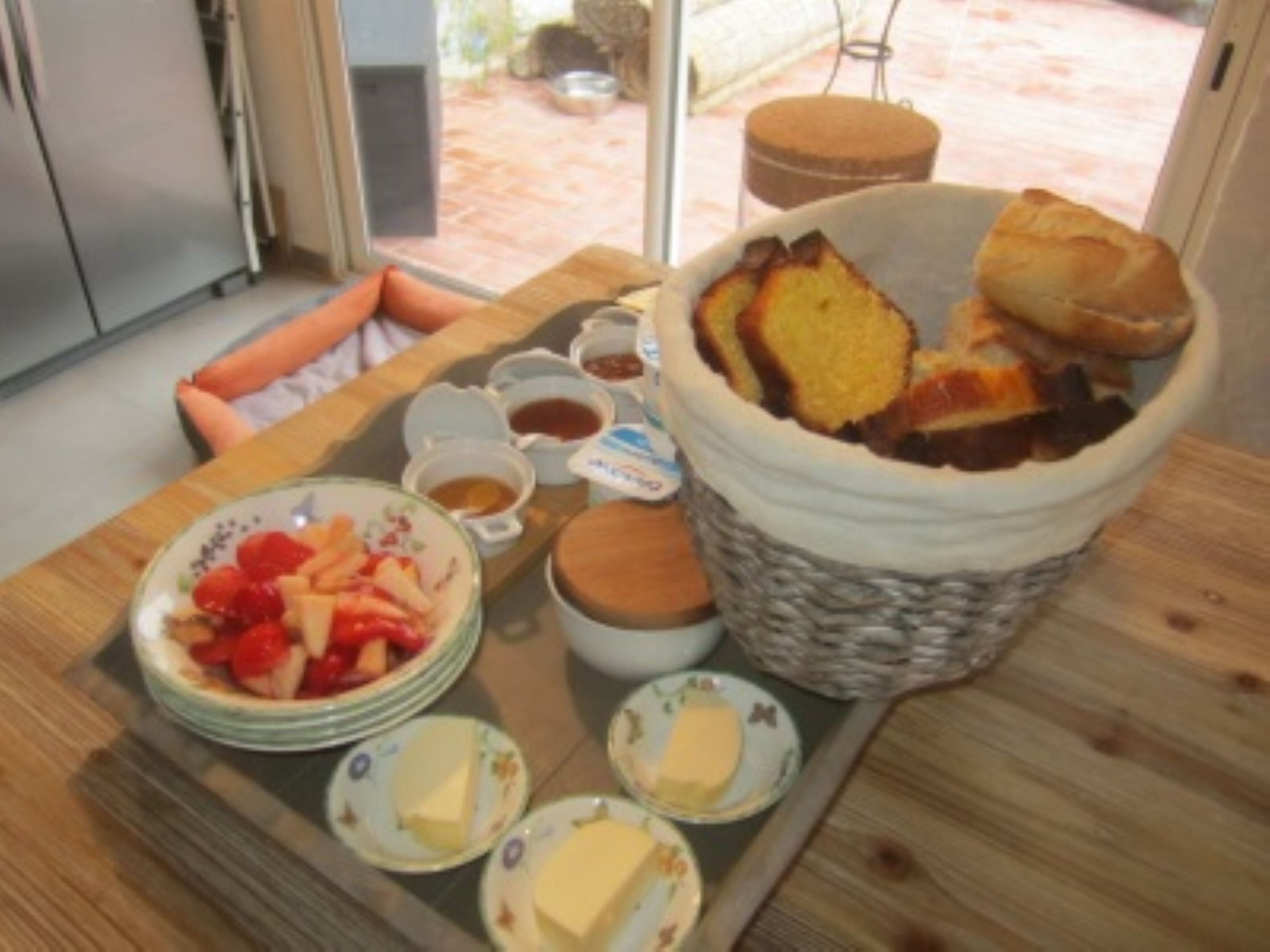 A breakfast tray with bread, butter, jam, and fruit on a wooden table.