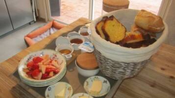 A breakfast tray with bread, butter, jam, and fruit on a wooden table.
