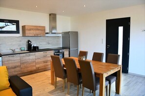 A modern kitchen with wooden cabinets, a built-in oven, and a stainless steel refrigerator. There is a dining table with chairs and a black door in the background. - Cosy sea view (OLMETO)