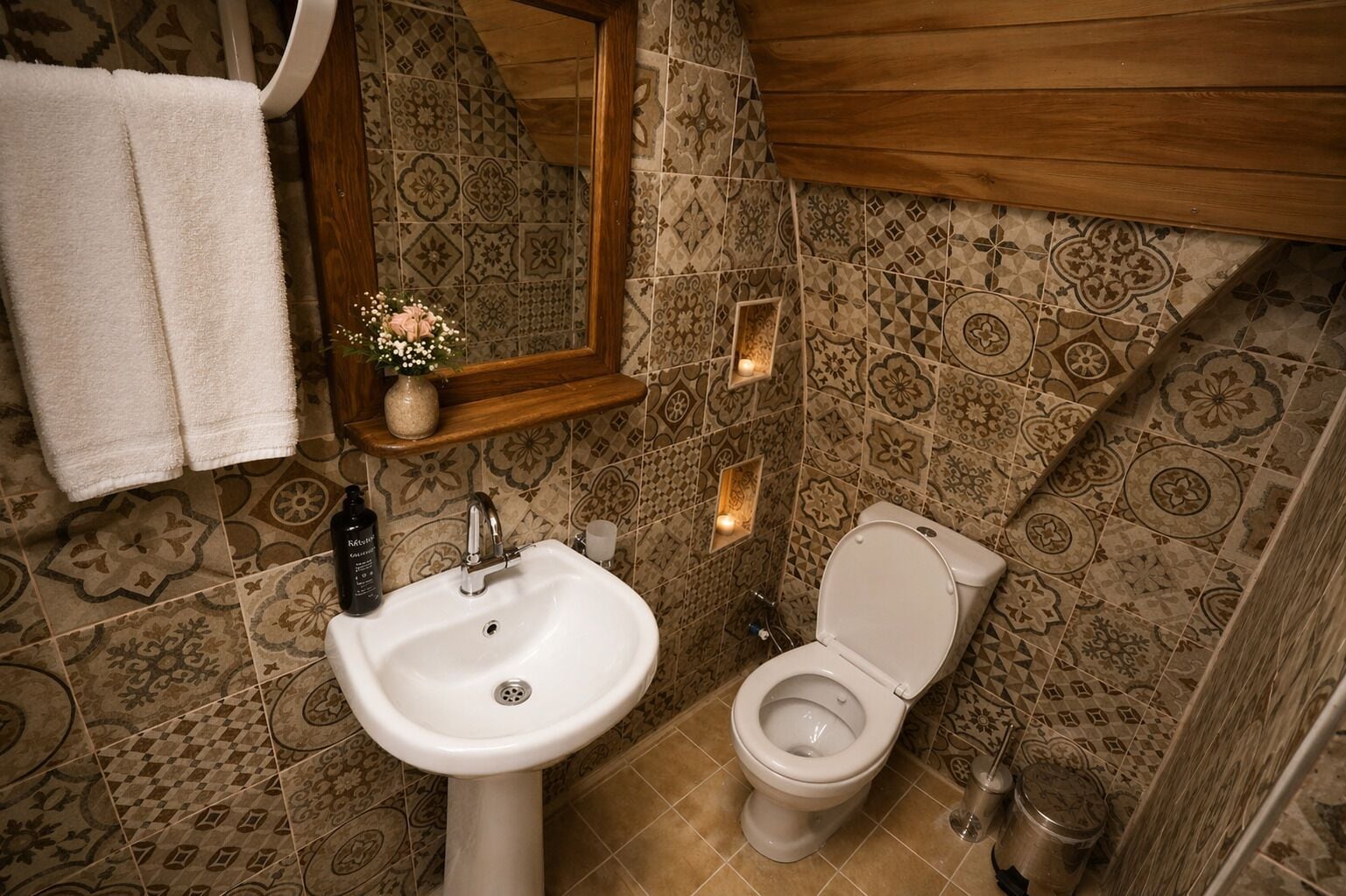 Une salle de bain avec des carreaux décorés, un lavabo, des toilettes, un miroir et un porte-serviettes.