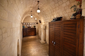 A stone-walled corridor with a wooden desk, hanging lights, and a large wooden cabinet. - Palmyra Boutique Hotel (Sanliurfa)