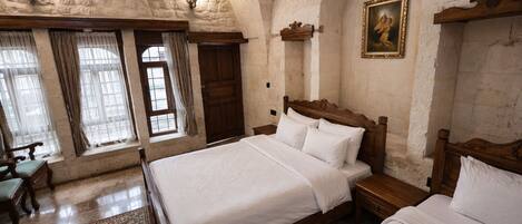 A bedroom with two beds, a wooden headboard, a painting, and a large window with curtains.