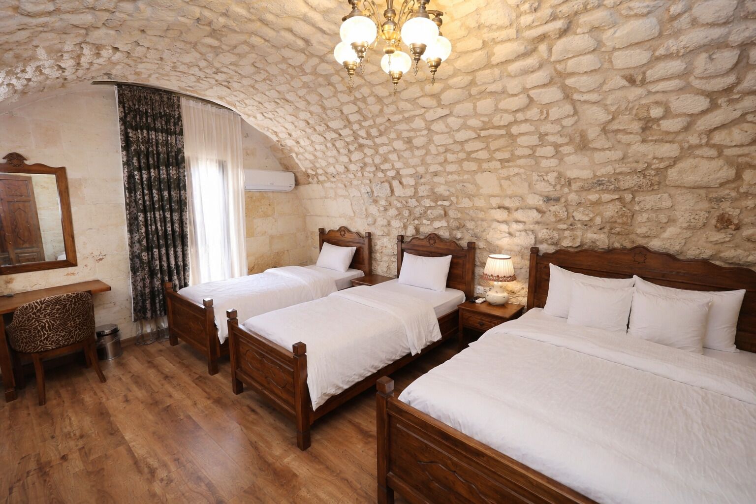 Una habitación con cuatro camas de madera, una pared de piedra, un escritorio de madera y un candelabro.