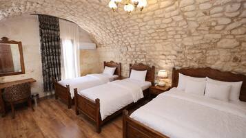 Una habitación con cuatro camas de madera, una pared de piedra, un escritorio de madera y un candelabro.
