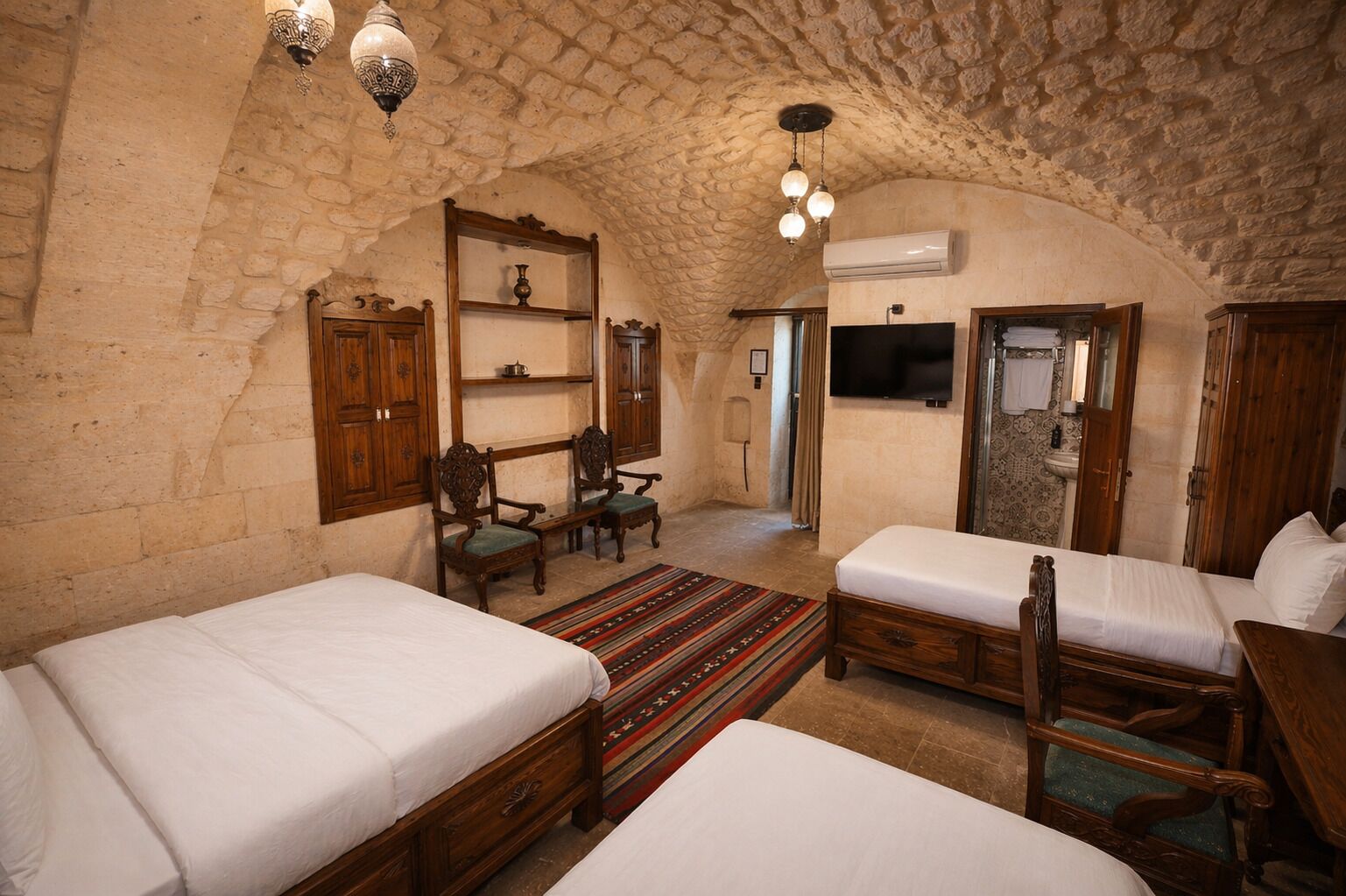 A room with two beds, a wooden wardrobe, a shelf with decorative items, a television, and an air conditioning unit.