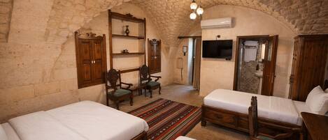 A room with two beds, a wooden wardrobe, a shelf with decorative items, a television, and an air conditioning unit.
