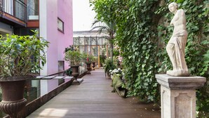 A corridor with a glass greenhouse, potted plants, and a statue. - Numa Berlin Belfort (Berlin)
