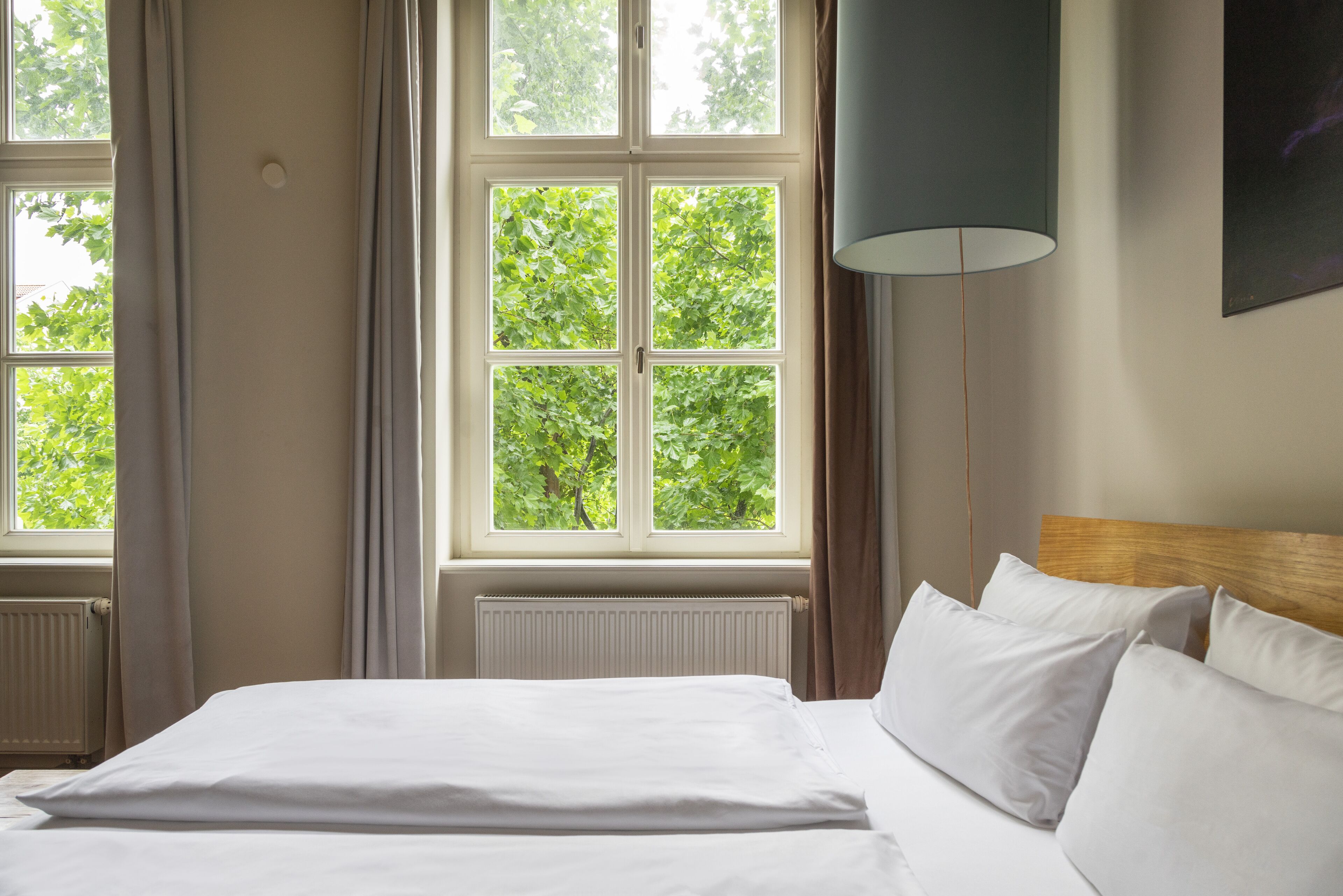 Una habitación de hotel con una cama grande, una ventana con cortinas, un radiador y una lámpara fijada a la pared.