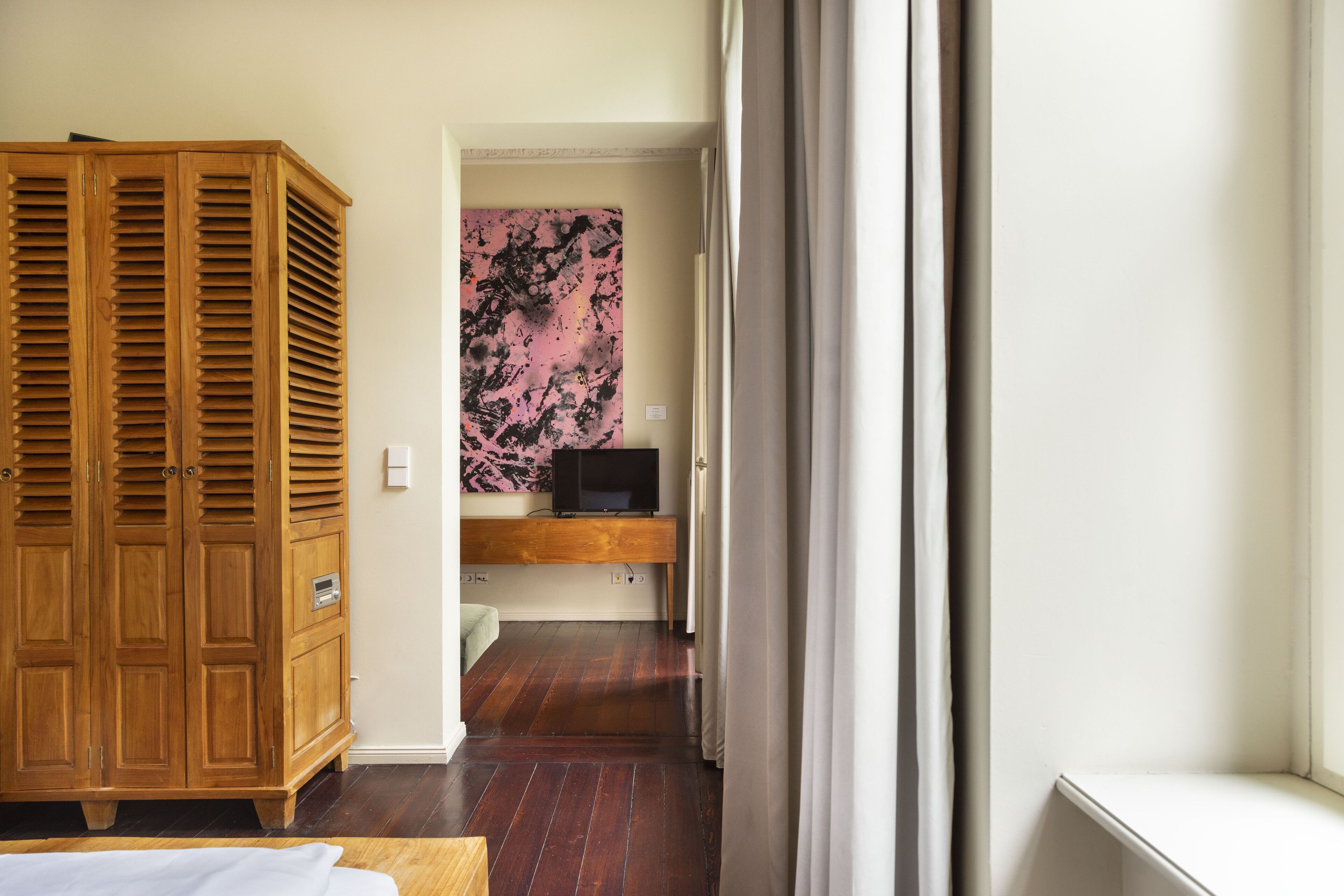 Ein Hotelzimmer mit einem Holzschrank, einem Fernseher auf einer Ablage und einem Fenster mit Vorhängen.