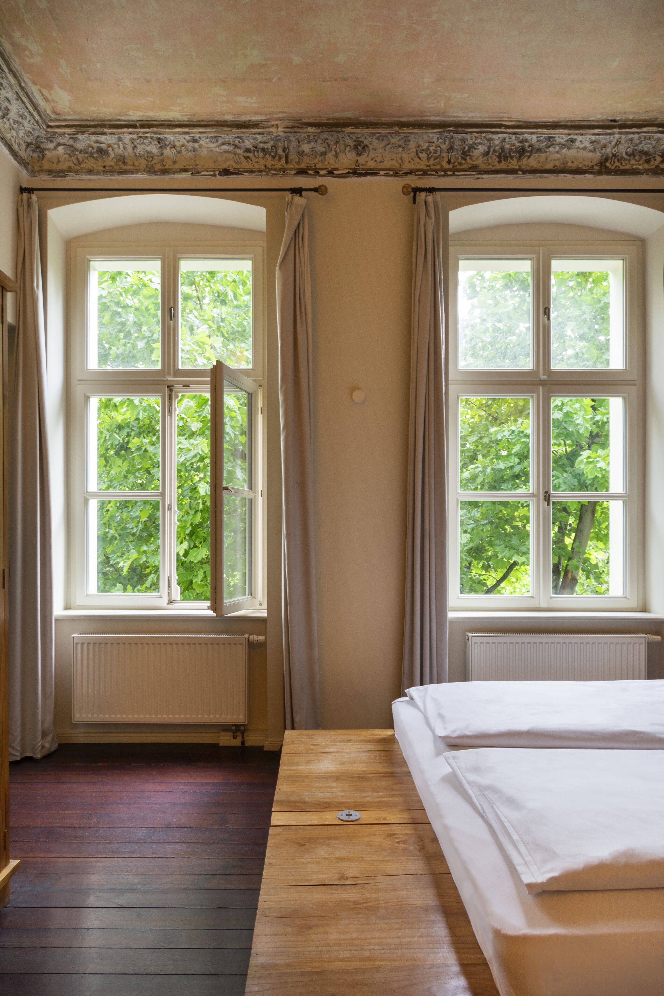 Una habitación con dos ventanas, una cama de madera y un radiador.