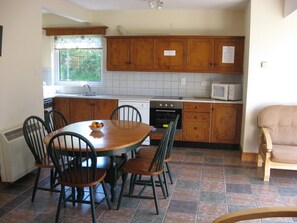 A kitchen with a dining table, chairs, a microwave, and cabinets. - Seamount Holiday Village No 24 (Courtown)