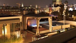Eine Dachterrasse mit Sitzgelegenheit, einer Feuerstelle und Blick auf eine Stadtlandschaft, einschließlich eines markanten Kuppelgebäudes.