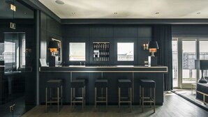 Eine moderne Bar mit dunkler Farbgestaltung, Barhocker und Blick auf die Stadt durch große Fenster.
