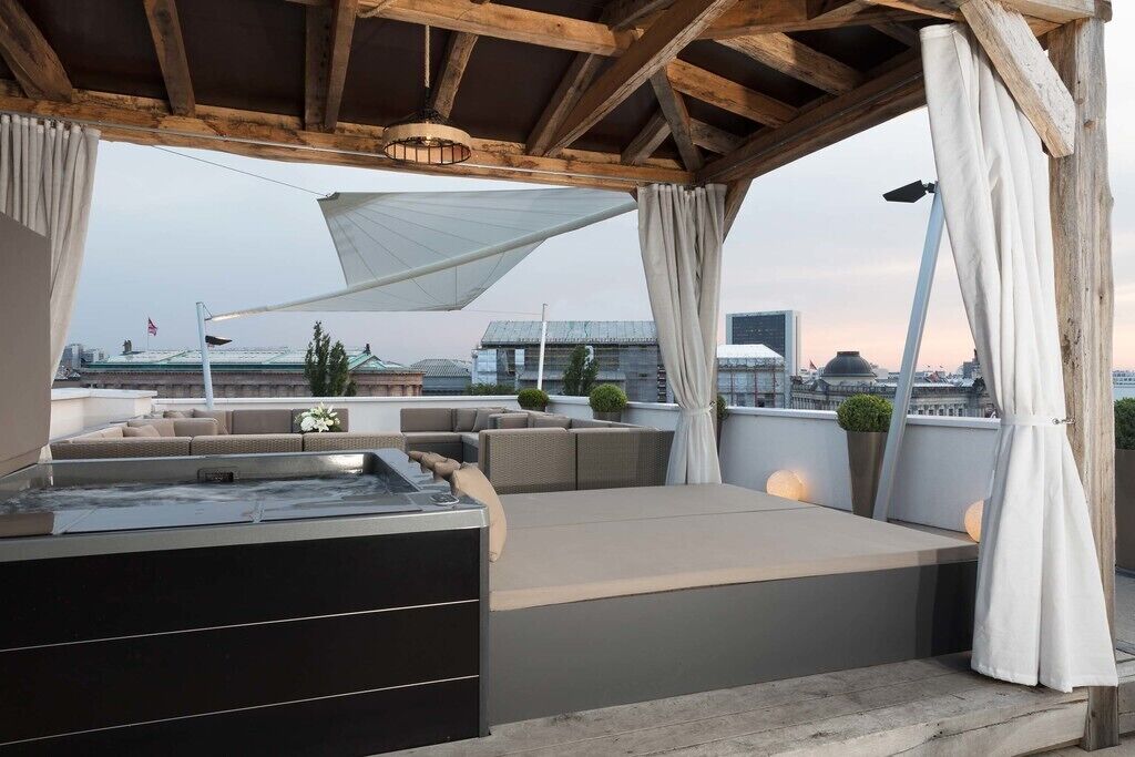 A rooftop terrace with a hot tub, seating area, and a view of the cityscape.