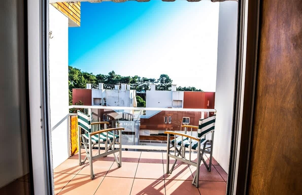 Ein Balkon mit Glastür, Fliesenboden und Blick auf Gebäude und Bäume.