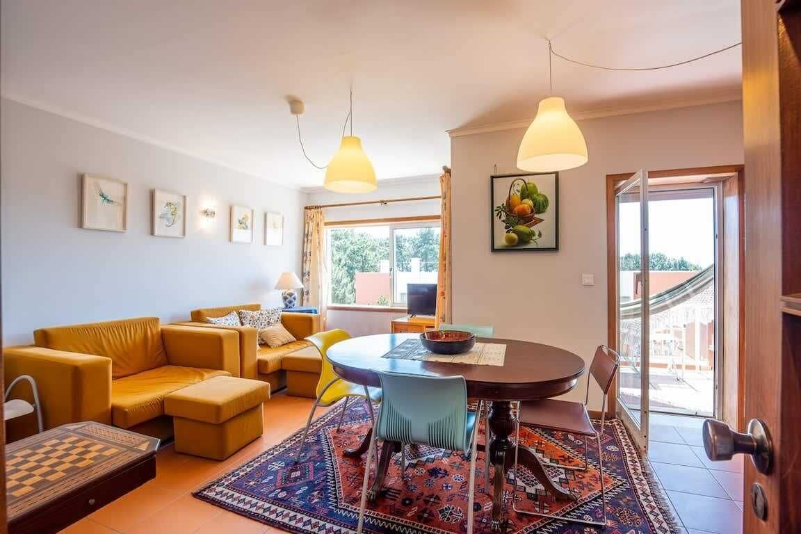 Una sala de estar con un sofá, una mesa de comedor, sillas, alfombra y obras de arte en las paredes.
