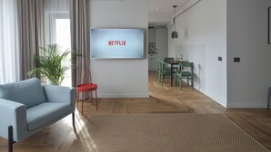 A modern living room with a light blue sofa, a red chair, a TV displaying 'NETFLIX', and a dining area with green chairs. - Atlas Aparthotel (Piatra Neamt)