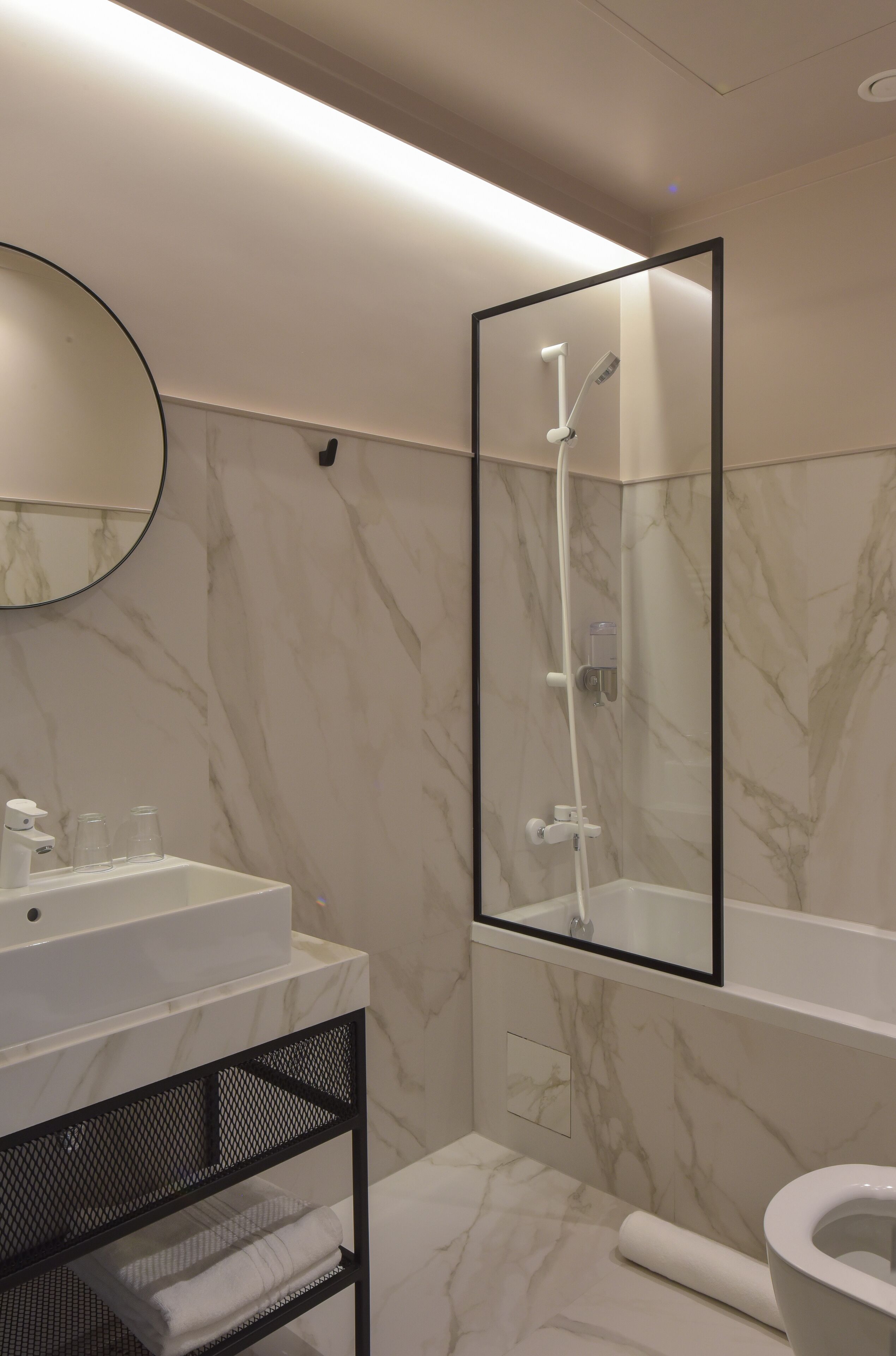 A modern bathroom with a marble wall, a white sink, a mirror, and a shower enclosure.