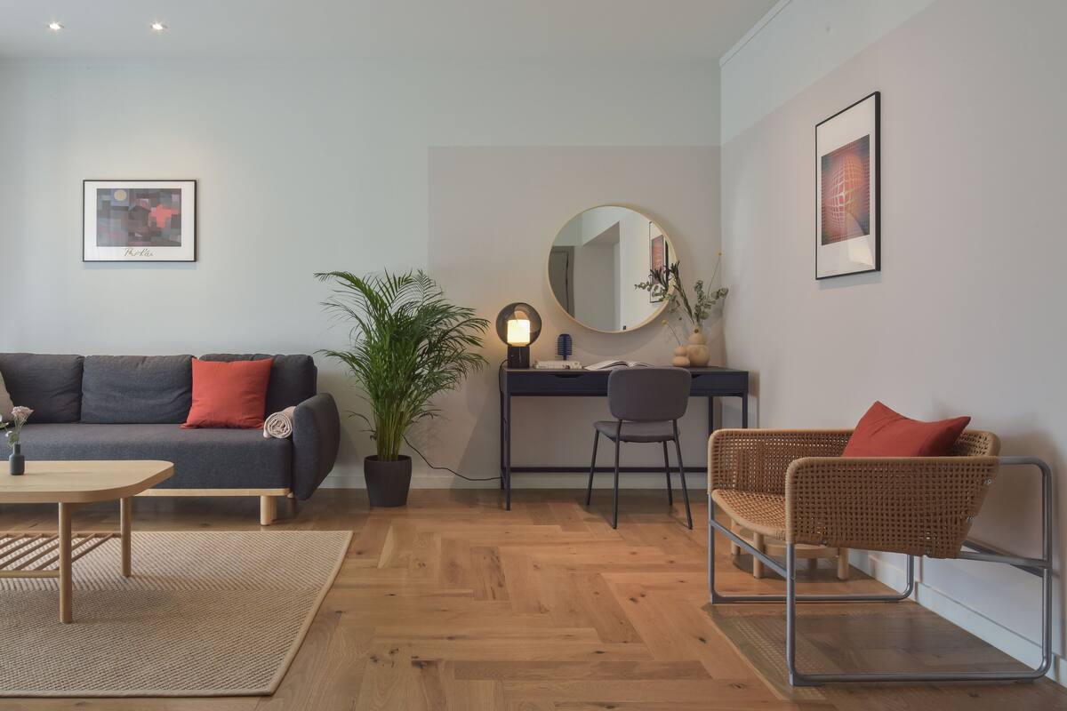 Ein modernes Wohnzimmer mit einer Couch, einem Couchtisch, einem Schreibtisch mit Stuhl und einem Korbsessel.