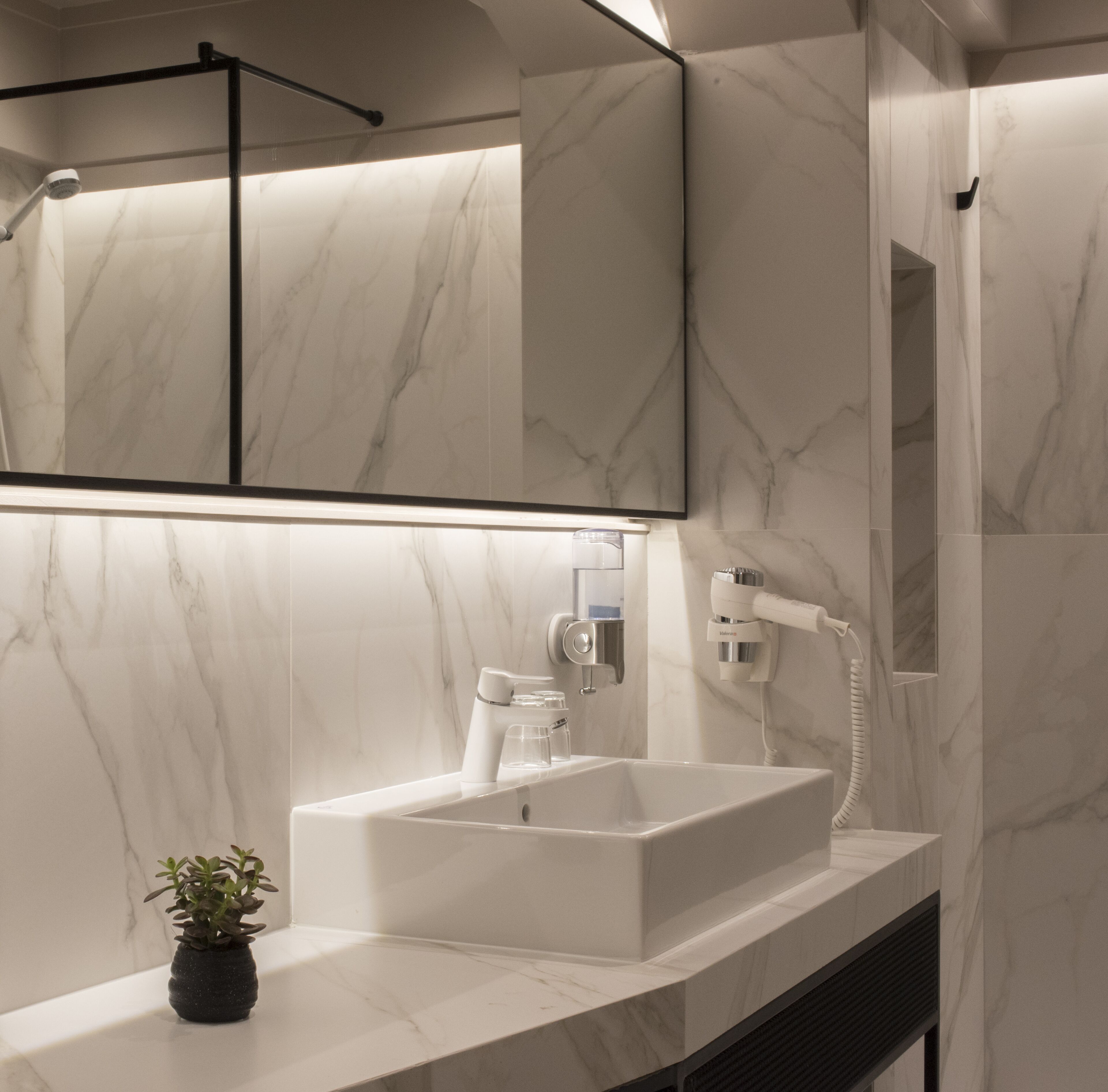 Een moderne badkamer met een grote spiegel, een witte wastafel en een handdouche.