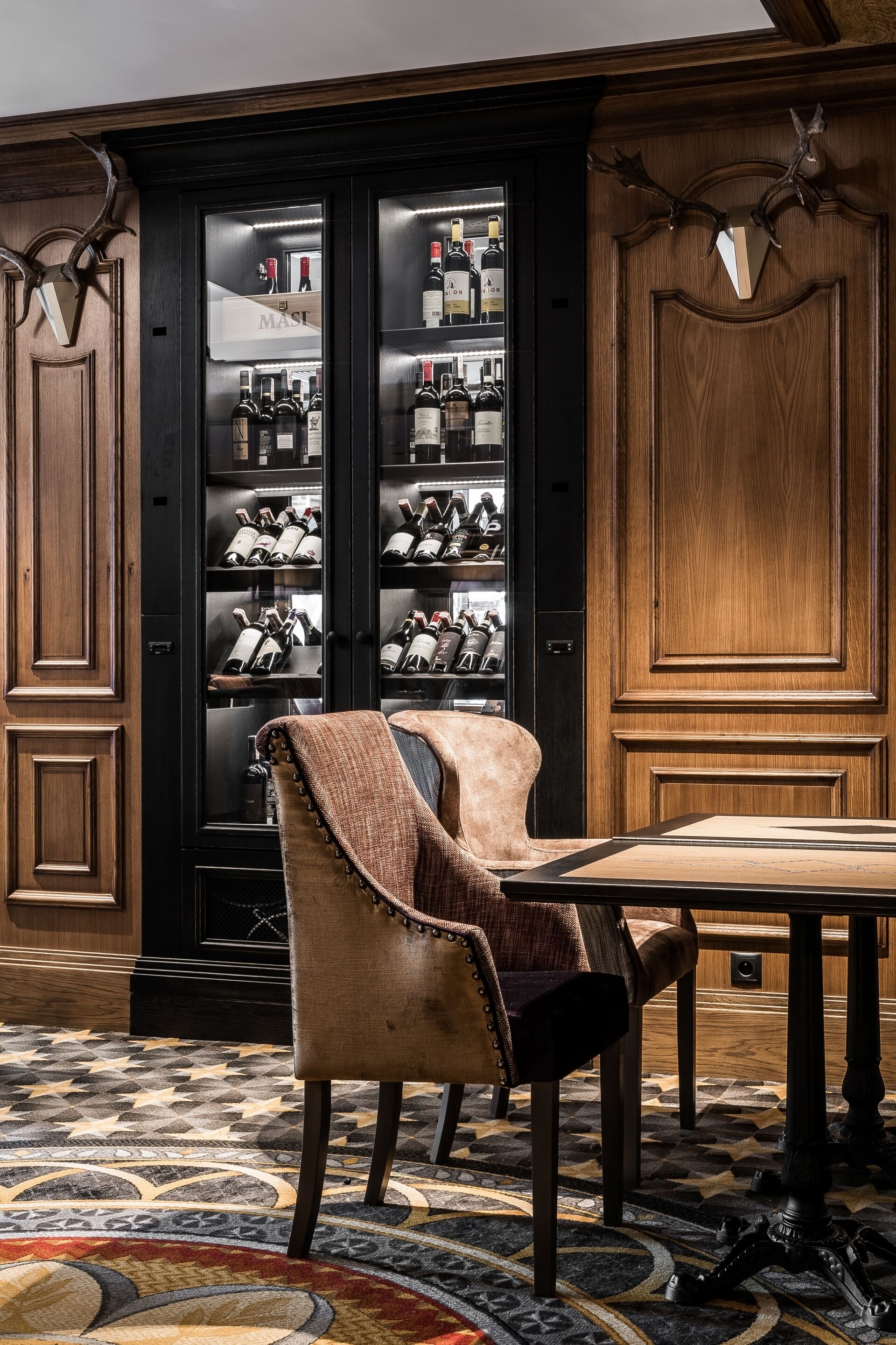 A room with a wooden cabinet displaying wine bottles, a leather armchair, and a patterned rug.