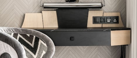 Una habitación de hotel moderna con un escritorio negro, dos lámparas fijadas a la pared, un televisor de pantalla plana y una alfombra estampada.