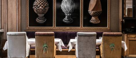 A dining area with a wooden panel wall, three framed vases, and four upholstered chairs with a patterned floor.