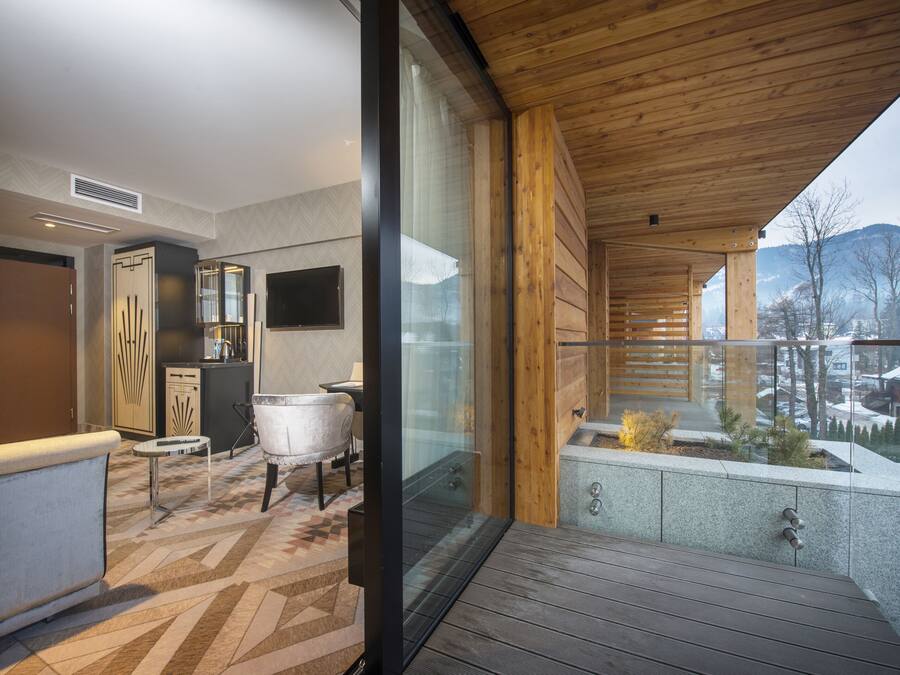 A modern interior with a wooden ceiling, a glass door leading to a balcony, and a view of snow-covered mountains.