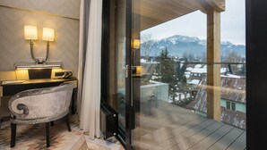 A modern hotel room with a view of mountains, a desk with a lamp, and a chair.