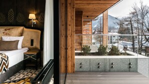 A modern hotel room with a bed, a nightstand, a lamp, and a balcony with a view of the city and mountains.