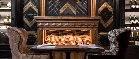 A bar area with a fireplace, two chairs, and a patterned floor.