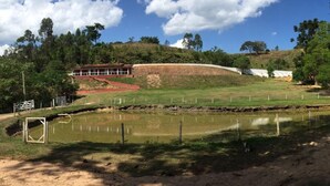 Un paysage rural avec un étang, une zone délimitée par une clôture et un bâtiment doté d’un toit rouge.