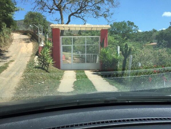 Une entrée fermée par un portail en métal, un chemin en béton et une végétation luxuriante tout autour.