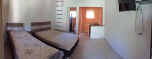 Une chambre avec deux lits, une petite kitchenette et une salle de bain visible par une porte ouverte.