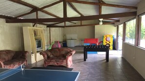 Un espace intérieur abrité comprenant une table de ping-pong, deux canapés et une table de baby-foot.