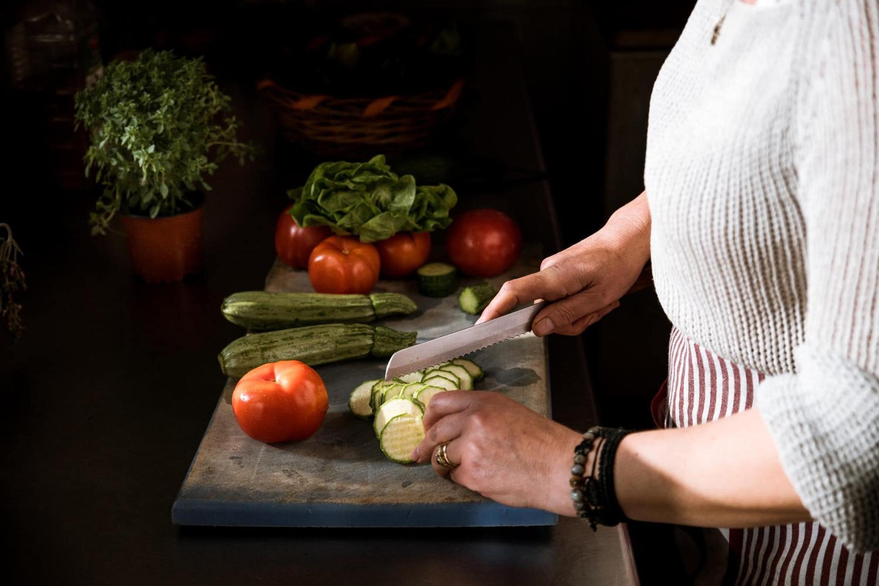 Una persona cortando verduras sobre una tabla de cortar.