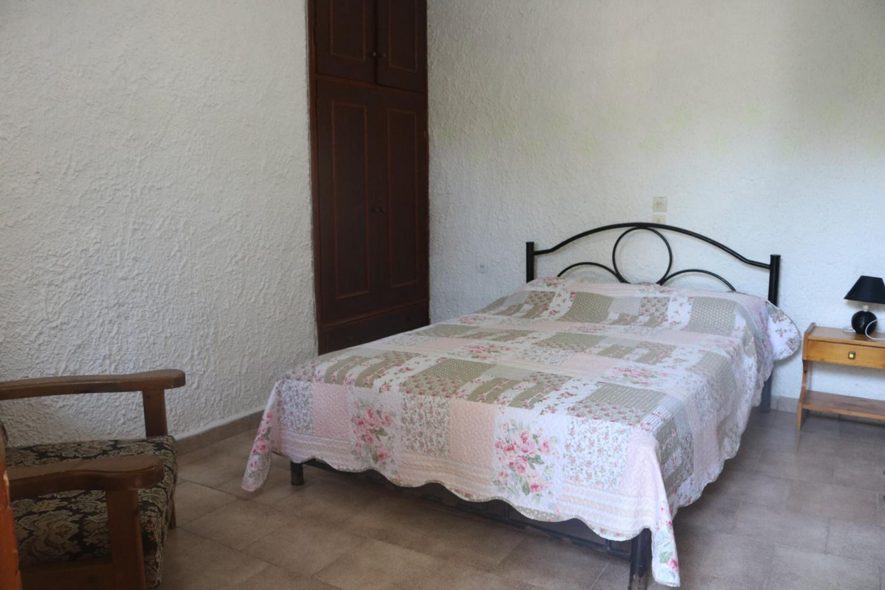 Een slaapkamer met een bed, een houten stoel, een nachtkastje en een kledingkast.