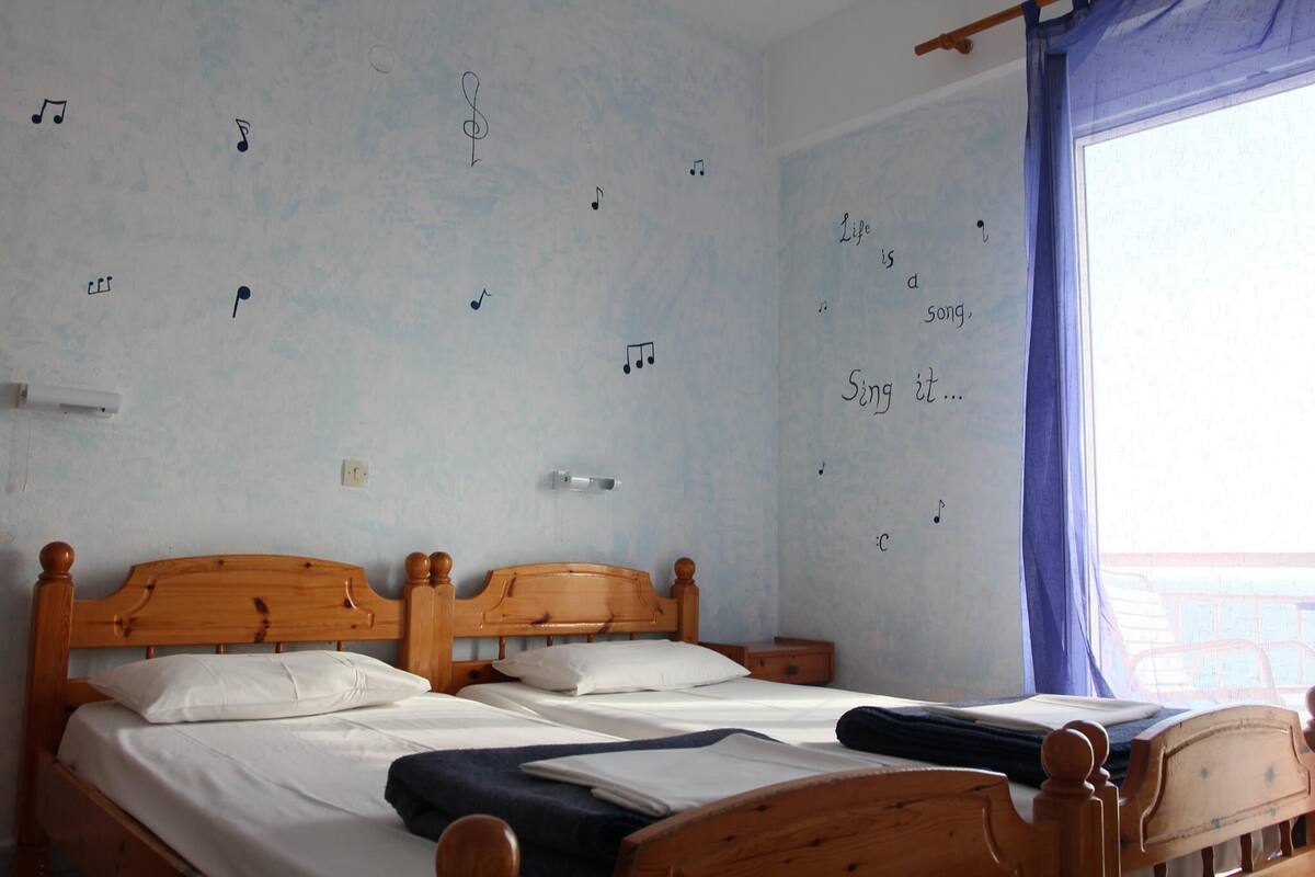 Una cama doble con cabecera de madera, una mesita de noche y una ventana con cortina.