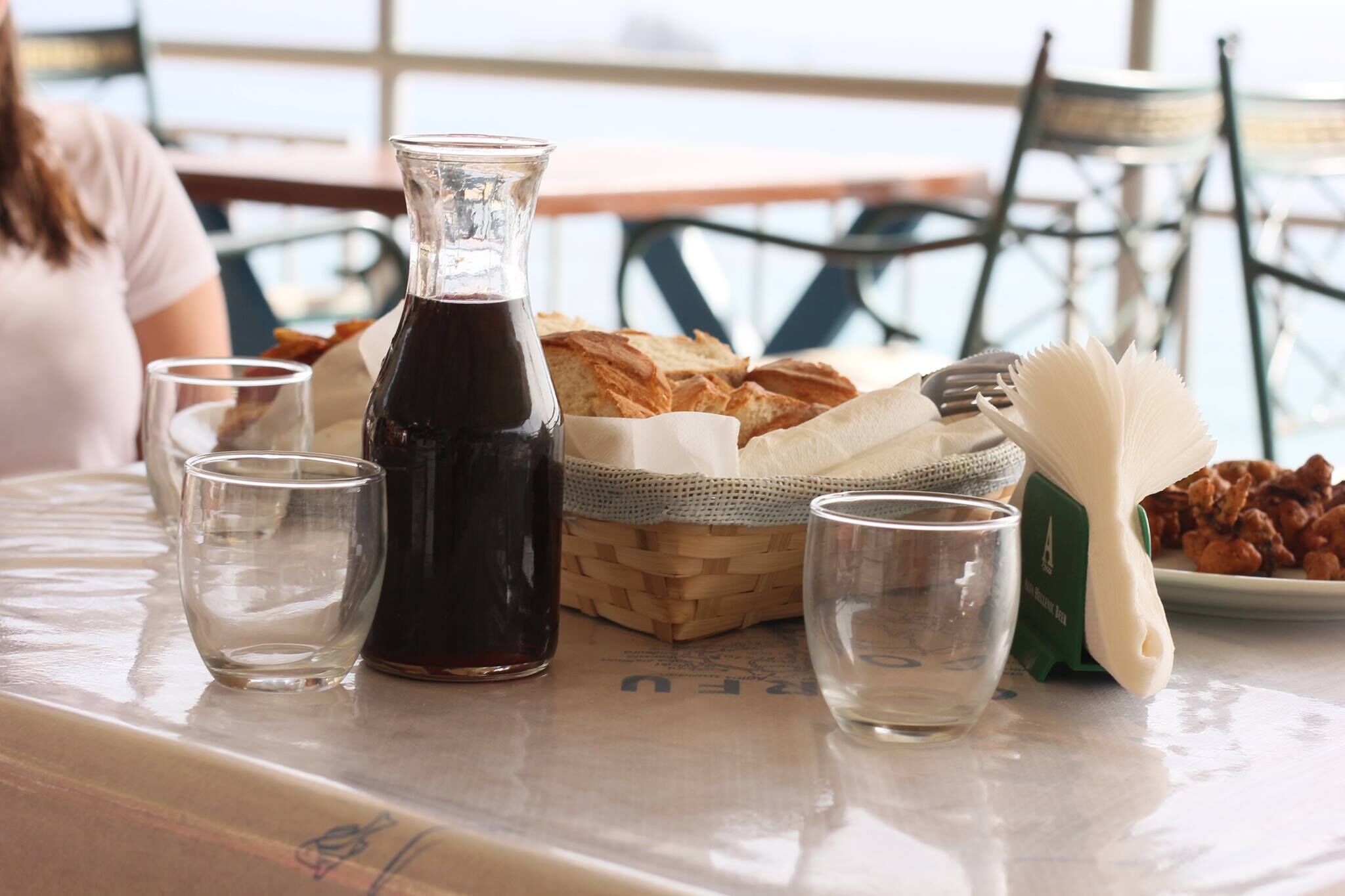 A table with a bottle of dark liquid, two glasses, a basket of bread, and a plate of nuts.
