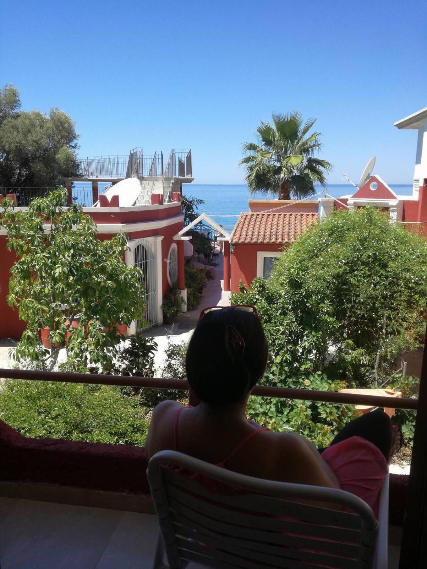 Uma varanda com vista para o mar e um edifício vermelho com varanda branca.
