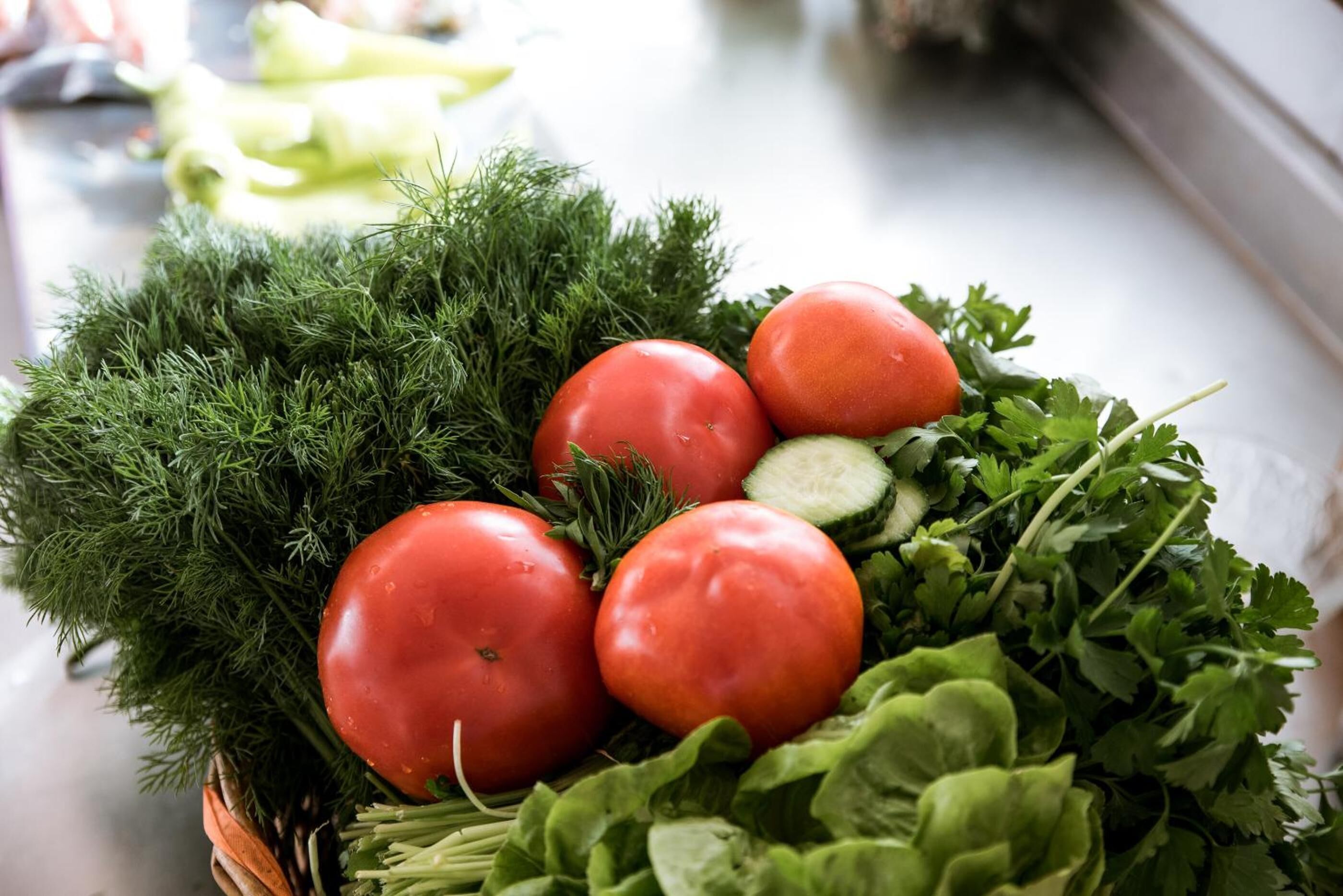 A basket of fresh vegetables including tomatoes, cucumbers, and leafy greens.