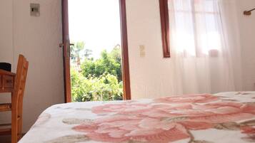 Un dormitorio con cama, una silla y vistas al verde exterior.