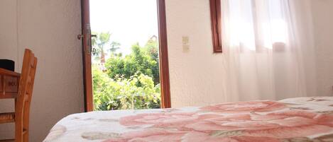 A bedroom with a bed, a chair, and a view of greenery outside.