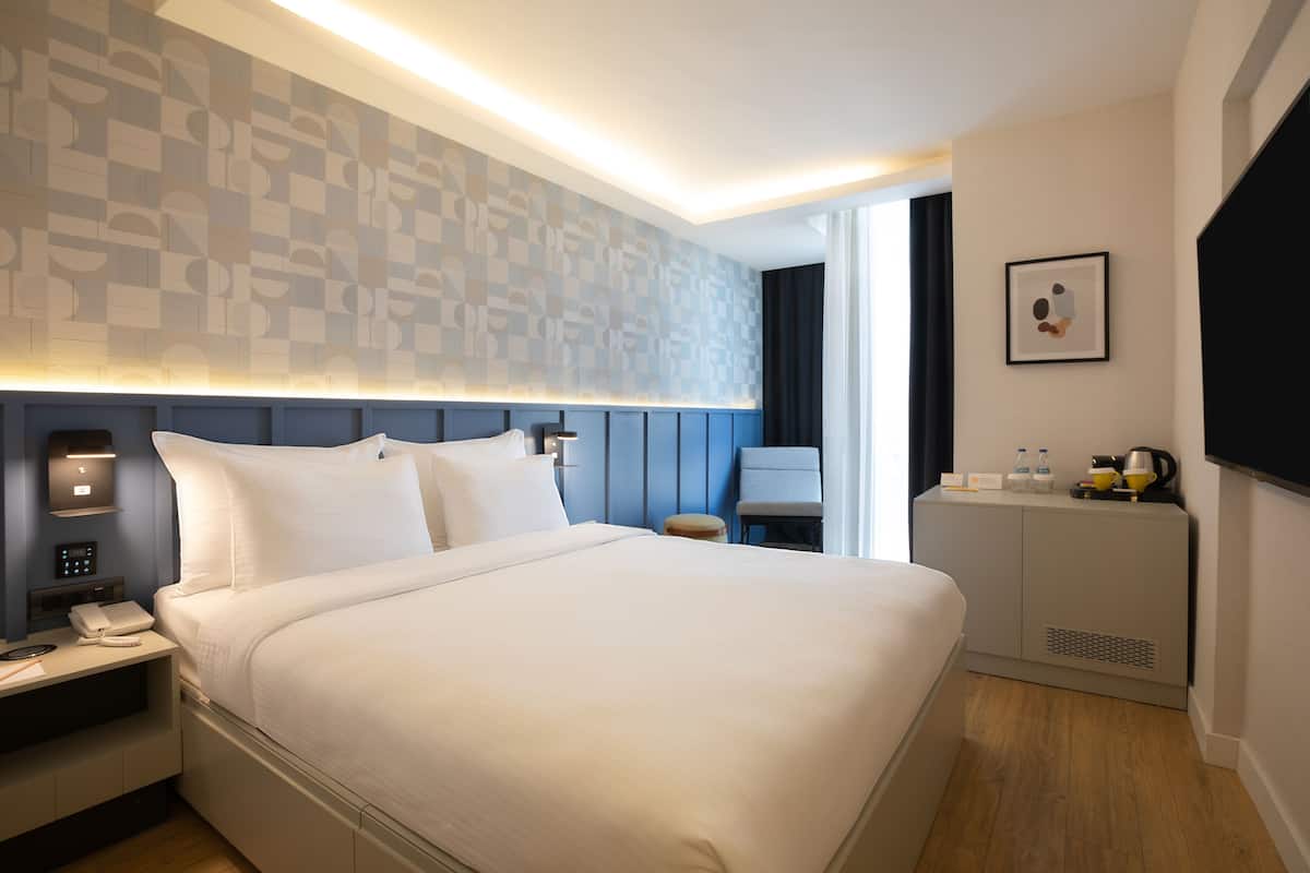 Een moderne hotelkamer met een groot bed, nachtkastje met telefoon en een klein bureau met stoel.