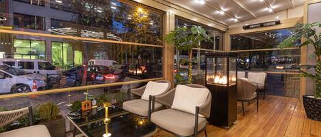 A modern indoor seating area with wooden flooring, glass walls, and a view of the street outside.