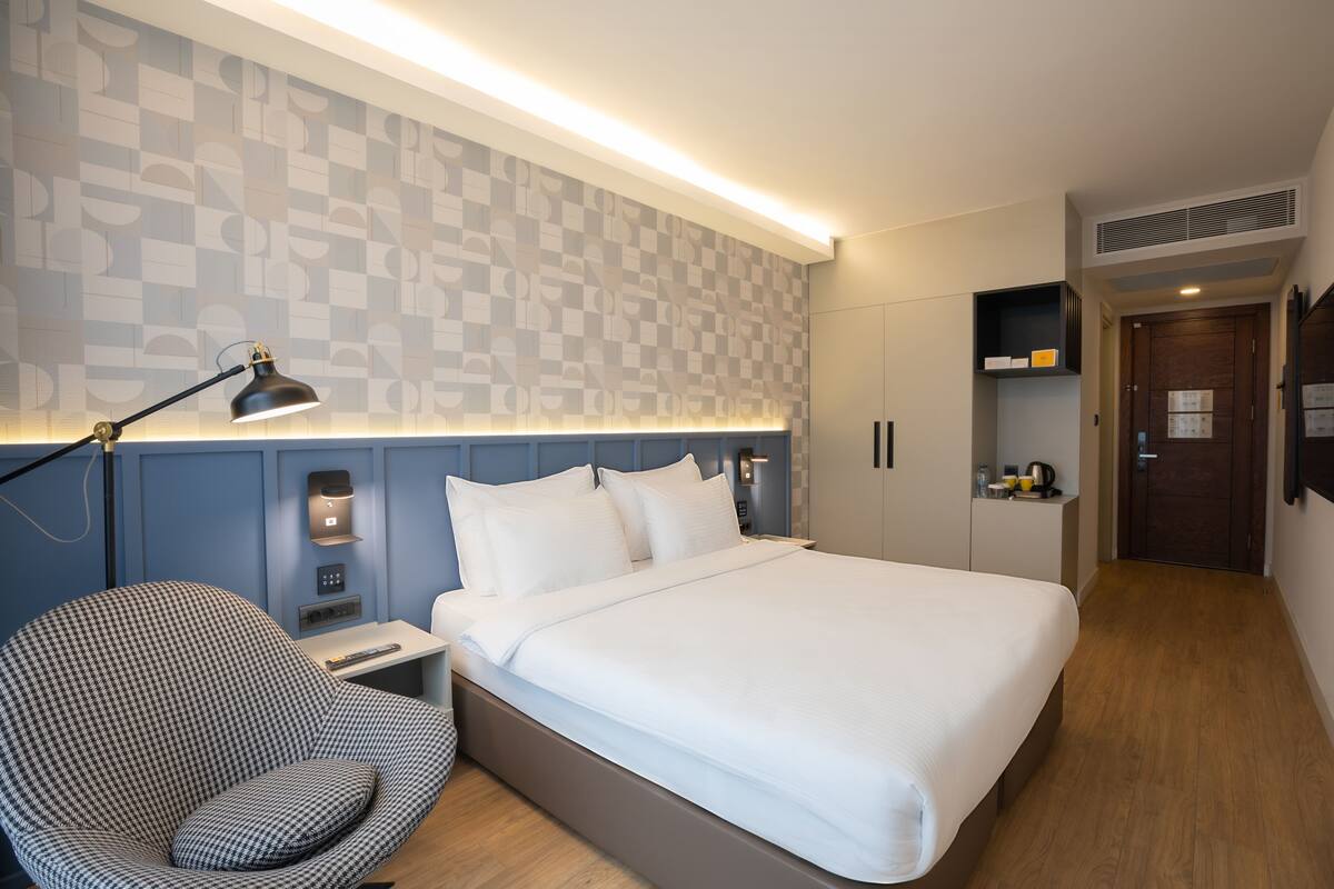 Een moderne hotelkamer met een groot bed, een bureau, een stoel en een aan de muur bevestigde televisie.