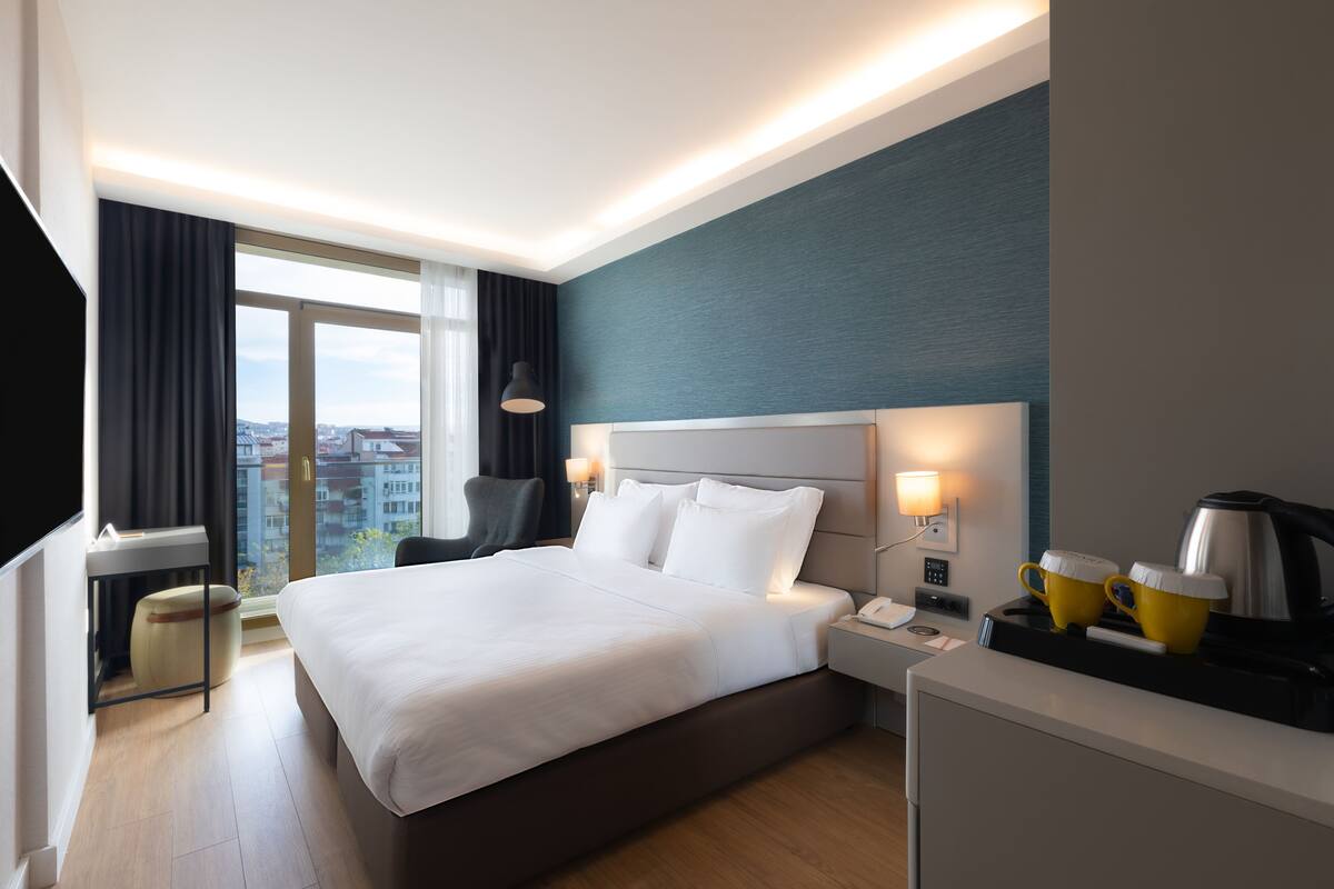 Een moderne hotelkamer met een groot bed, een bureau, een stoel en uitzicht op de stad.