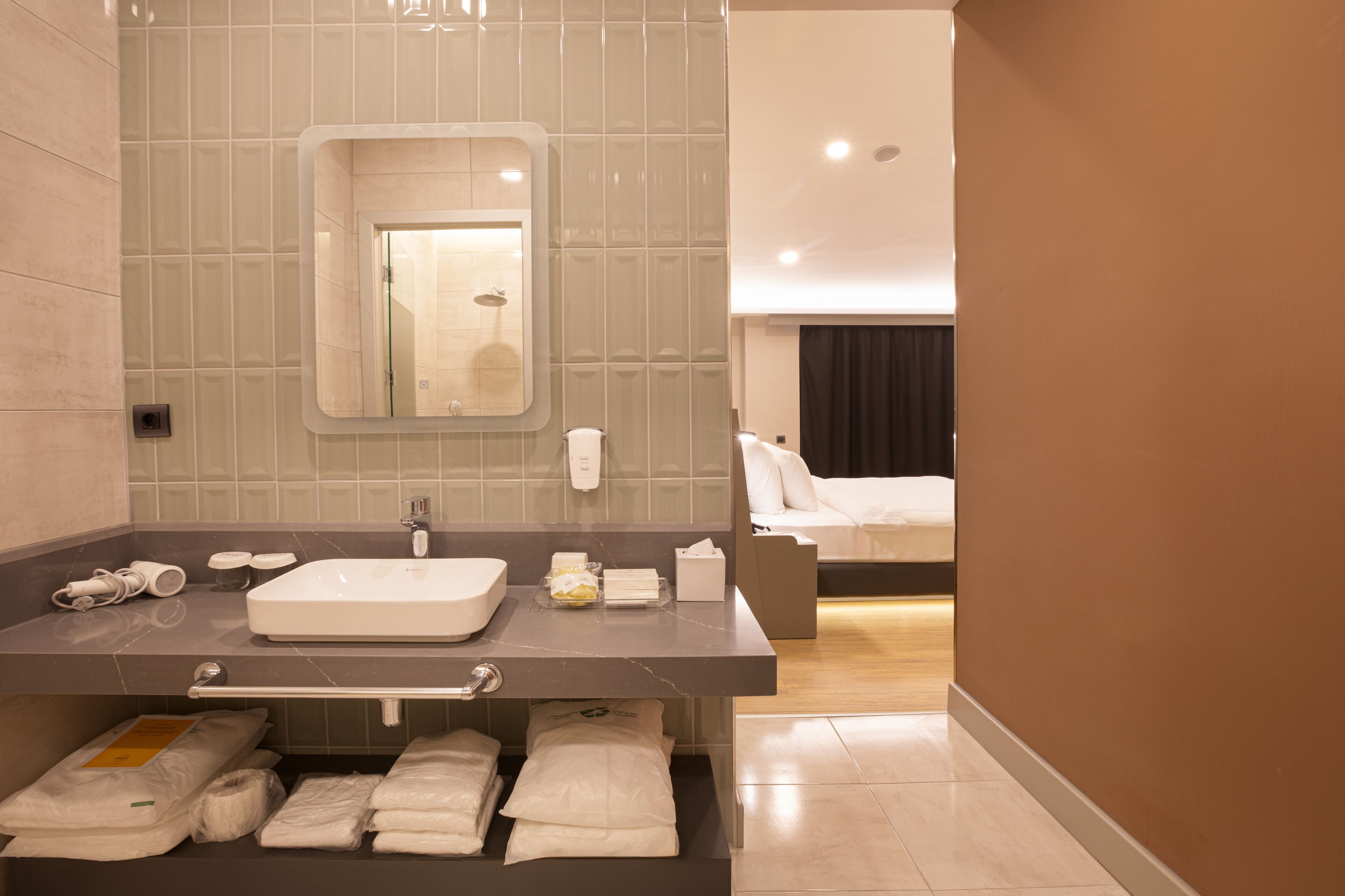 A modern bathroom with a large sink, mirror, and a shower visible in the reflection.