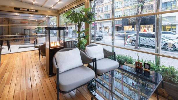Un intérieur moderne avec un plancher en bois, un coin salon doté de fauteuils confortables, une table en verre agrémentée d’objets décoratifs et une grande fenêtre donnant sur la rue.